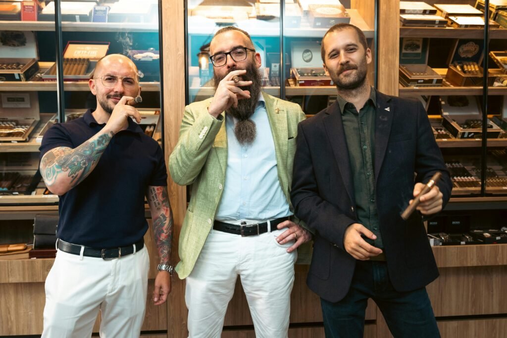 Three stylish men with tattoos pose confidently with cigars in a cigar store.